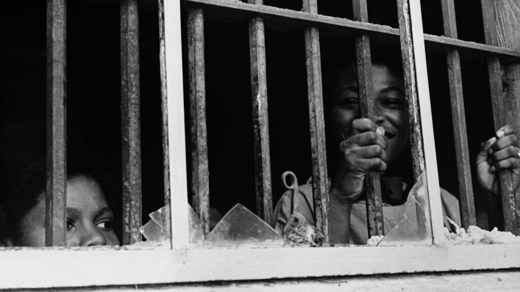 Two young black girls in a jail cell looking out window. Shirley Green holding the bars and smiling
